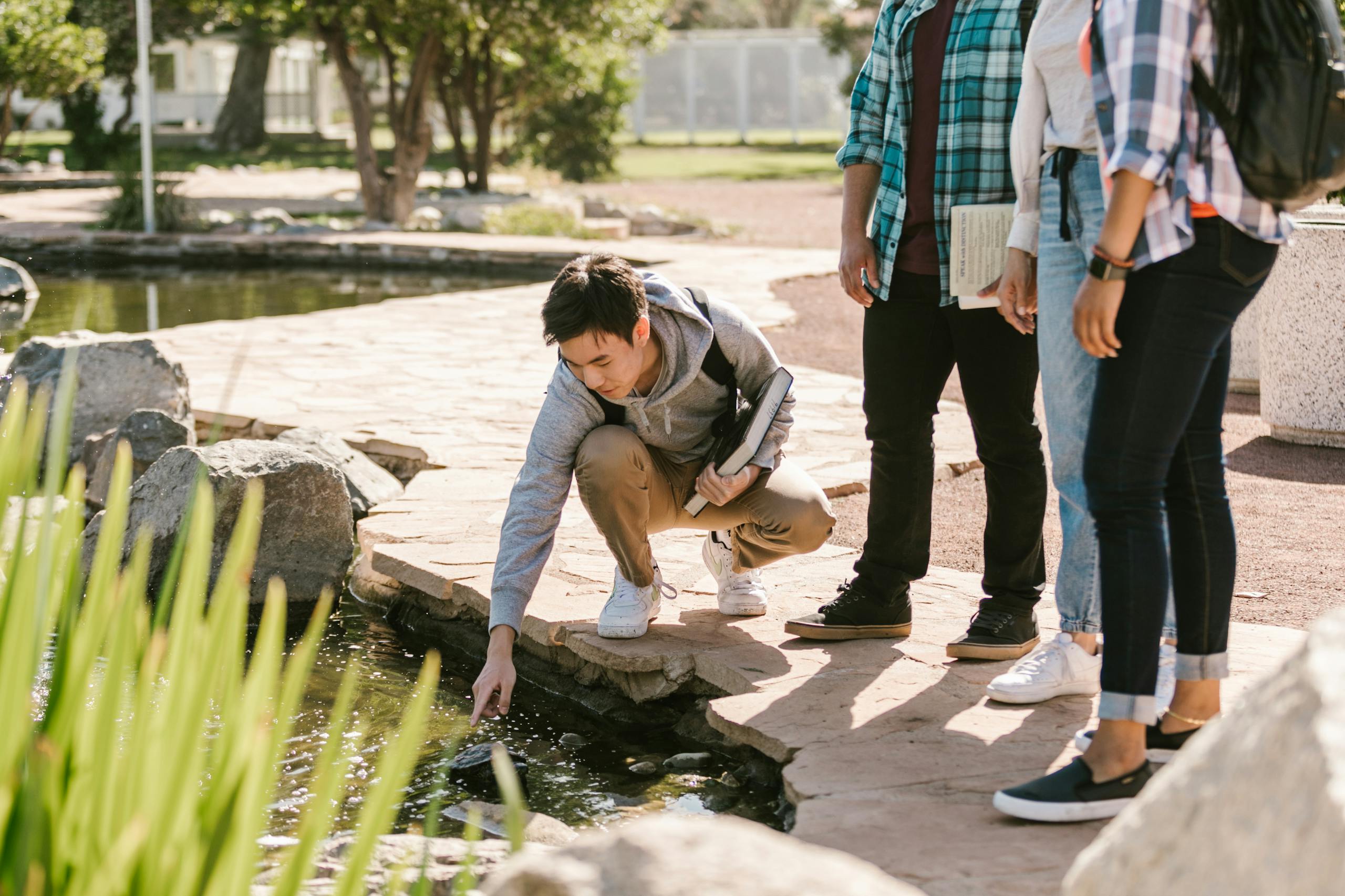 Group of college students interacting with pond nature during study session outdoors.